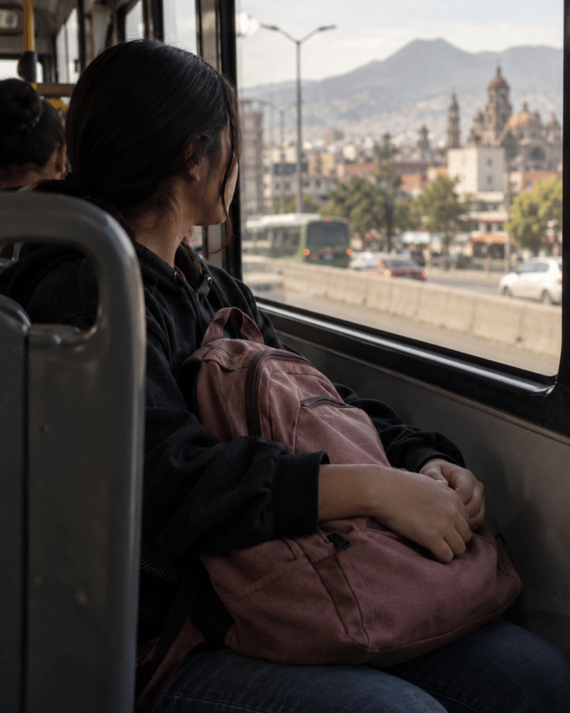 Adolescente con mochila mirando por la ventana de un autobús en una calle mexicana